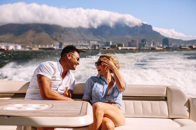 Cheerful young couple sitting on boat on sunny day