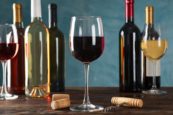 Corkscrew, bottles and glasses with wine on wooden table against blue background