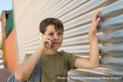 Boy having conversation on smartphone with hand on metal shutter 41QPZ4
