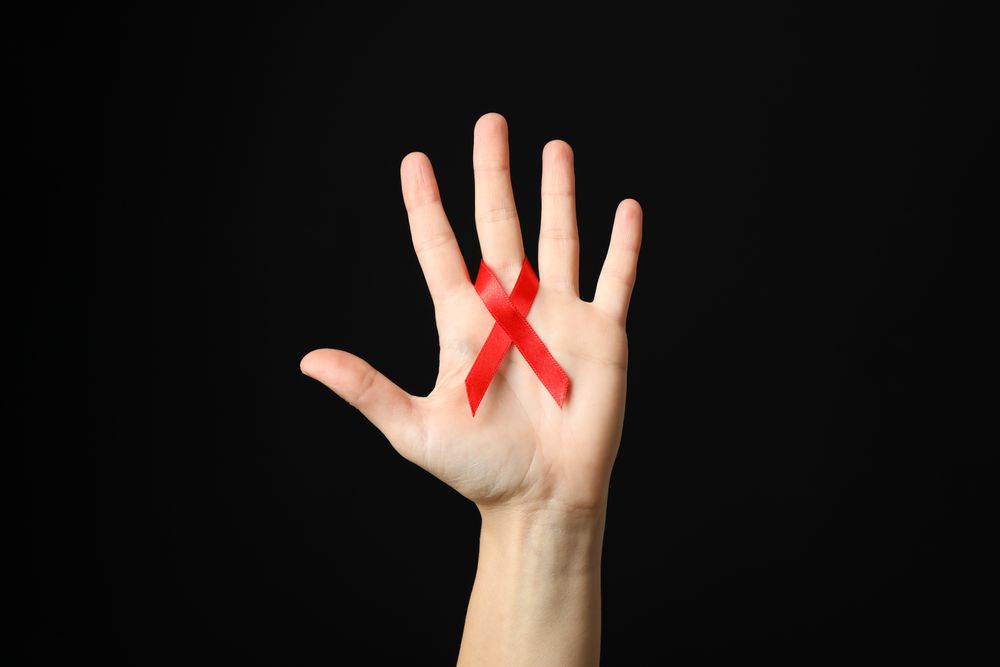 Hand and red awareness ribbon against dark background, space for text