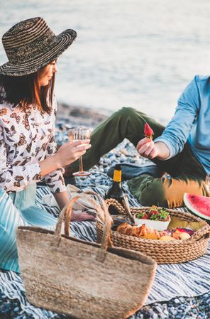 Couple having picnic by the ocean with man holding strawberry