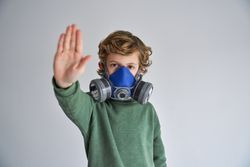 Calm child in respirator showing keep distance gesture in gray s