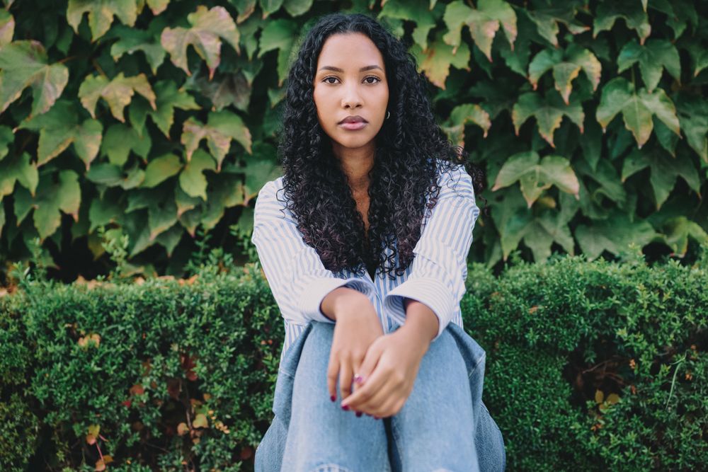 A contemplative young woman sits peacefully in lush greenery, embodying elegance and calm