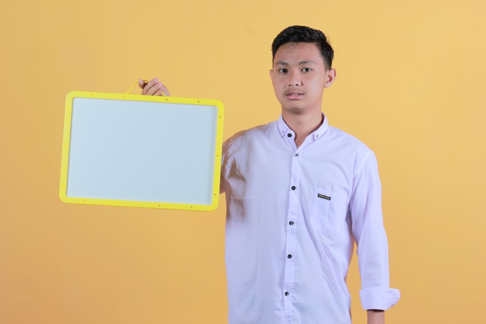 Portrait a young man in yellow backdrop holding a blank note board