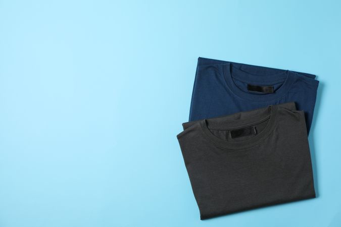 Folded blank t-shirts on blue background, space for text