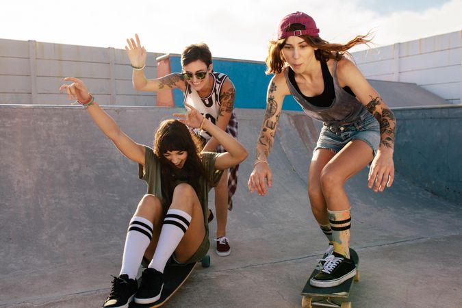 Three young women riding and skating on boards at skate park