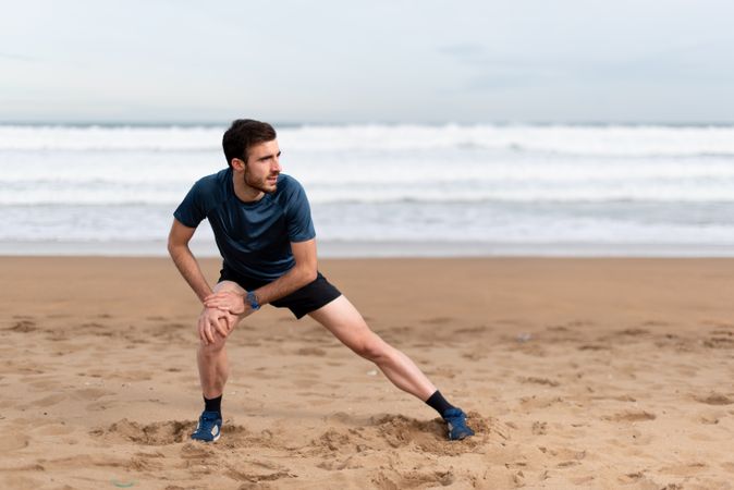 Male athlete in active wear doing exercises on legs at empty beach