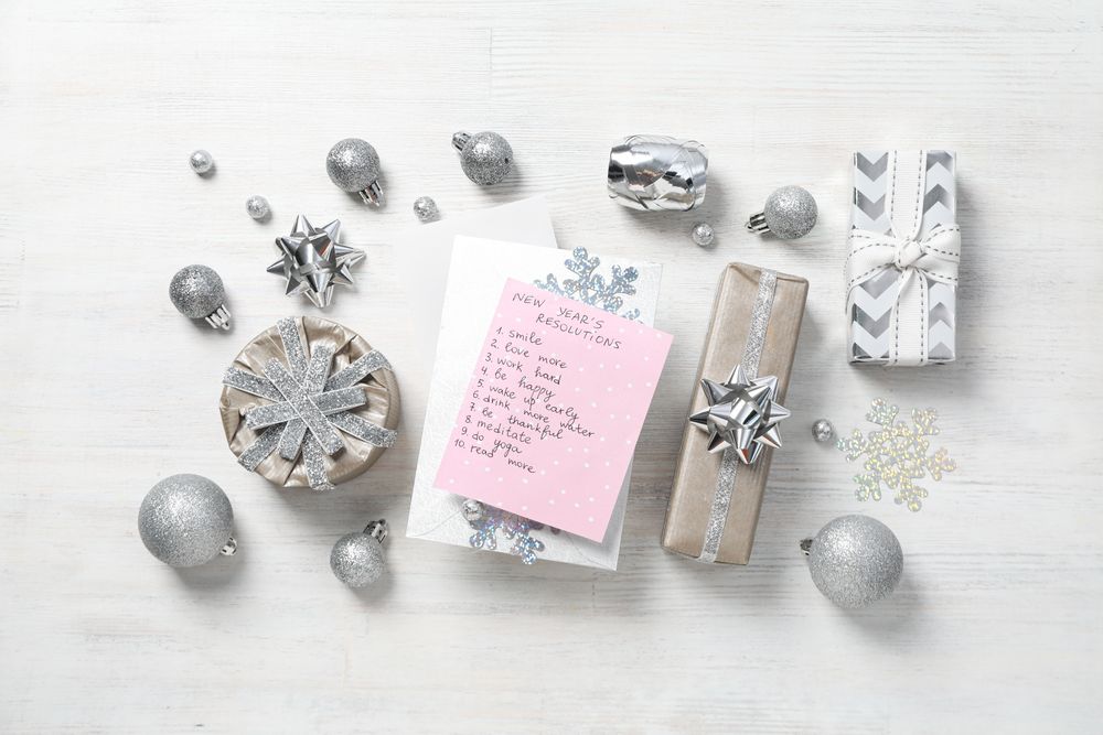 Notepad with list, decorations and gift boxes on light background, top view