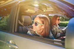 Happy young woman looking back through passenger window in car
