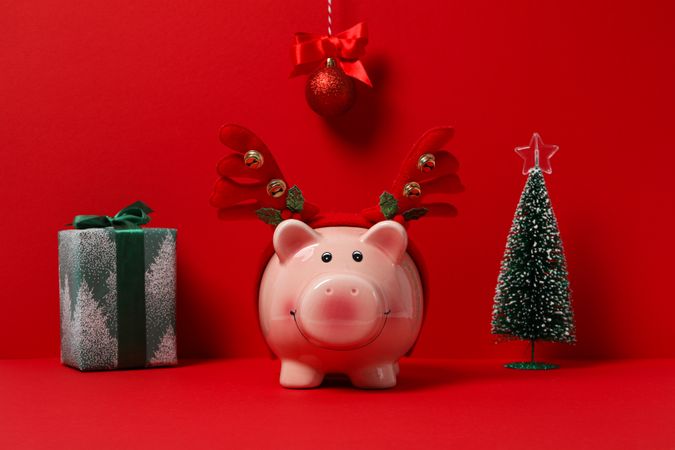 Piggy bank with Christmas decor and gift box on red background
