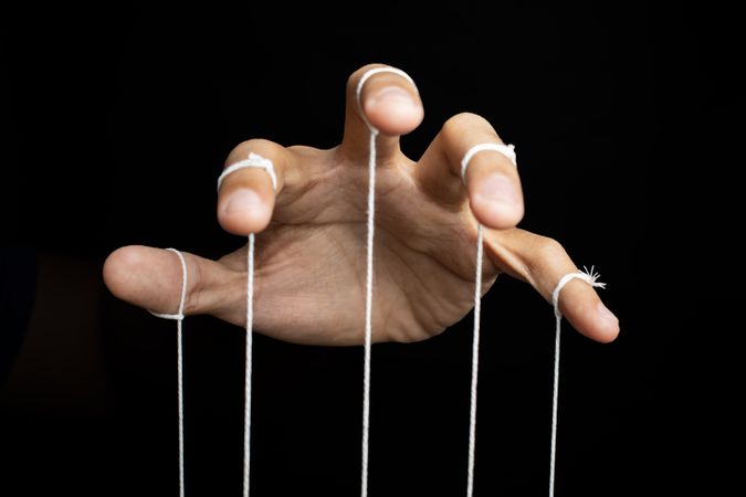male puppeteer hand with strings isolated on dark background.