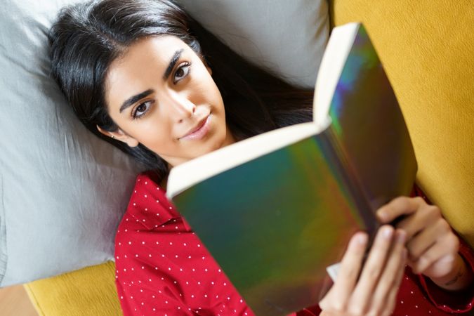 Woman lying on pillows with a green book