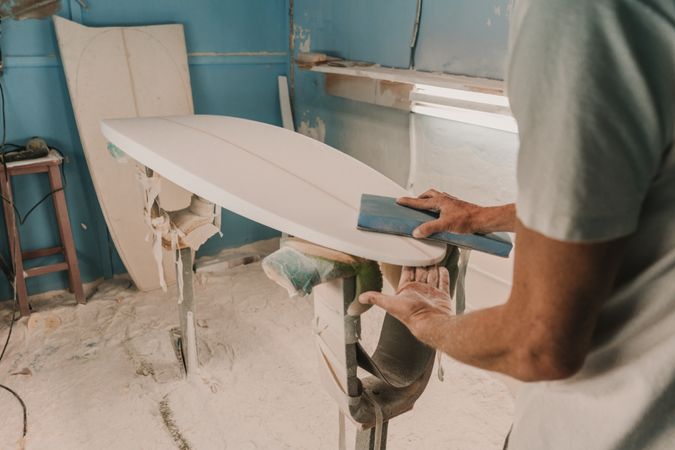 Man in respirator polishing surf board in workshop