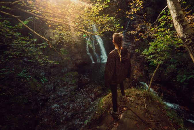 woman standing in a Small river and waterfall flowing in green dark beautiful forest.