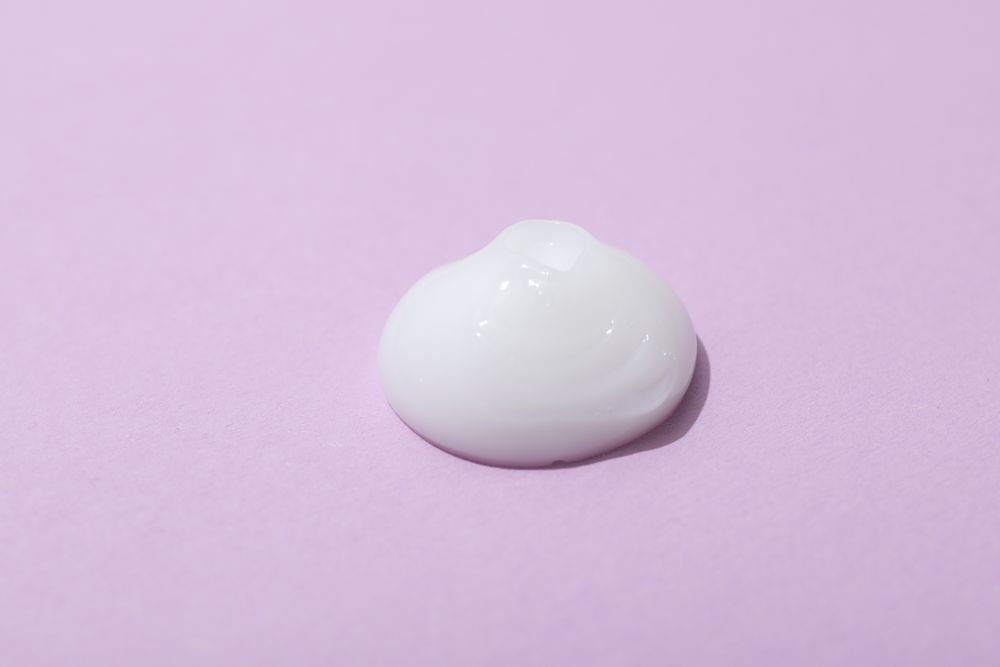 Drop of cream on pink background, close up