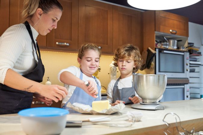 Girl with an apron cutting a piece of butter with a boy and a woman next to her