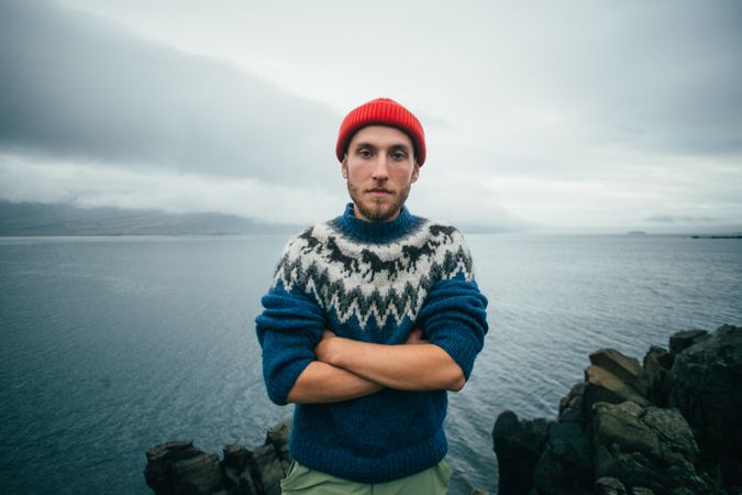 Portrait of man in woolen sweater on rugged Icelandic coast with his arms crossed