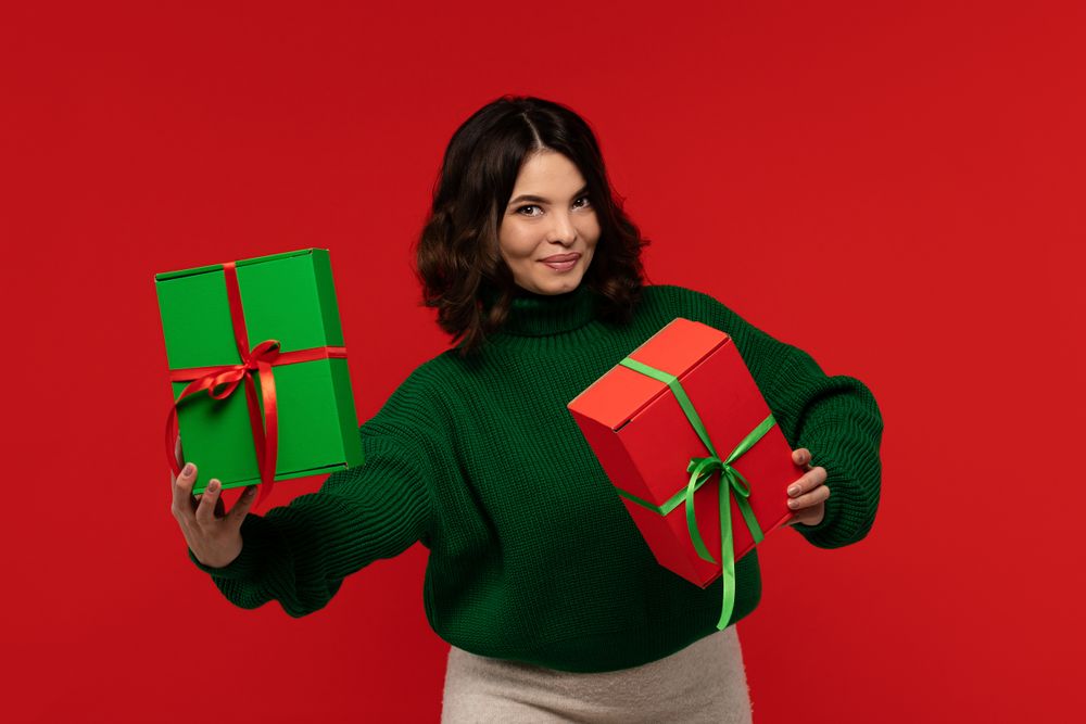Smiling woman in green sweater holding two wrapped gift boxes