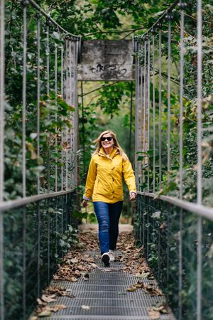 Cheerful female tourist standing on hanging bridge in summer