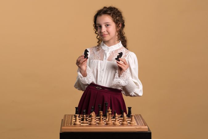 Young girl displaying two chess knights confidently.