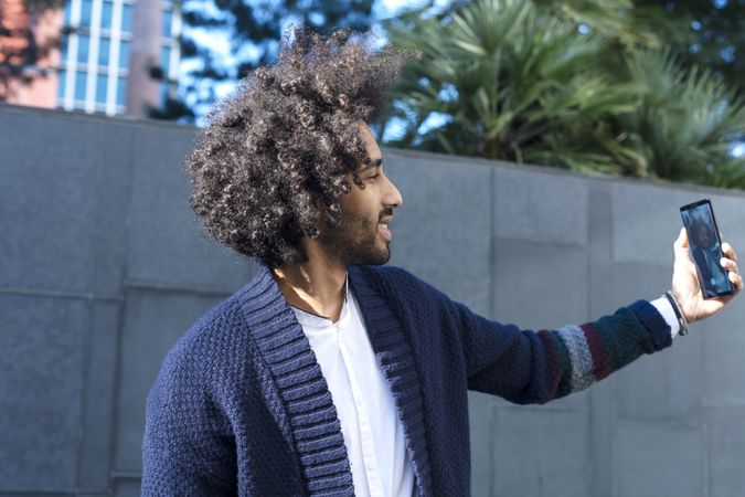 Smiling Black man in cardigan taking selfie outdoors in the sun
