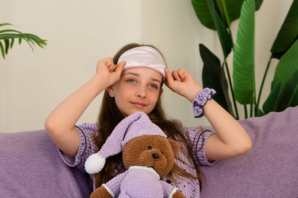 Smiling teenage girl with sleep mask and teddy bear