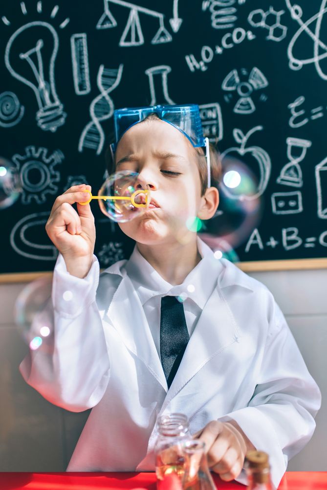 Kid blowing soap bubbles in front of drawings on chalkboard