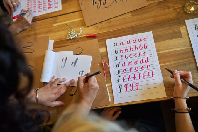 Crop faceless female students practicing lettering in classroom