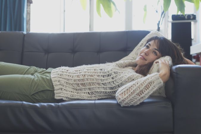 Female in wooly sweater lying on leather couch in living room
