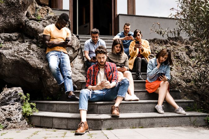 Millennial multi-ethnic friends group using smartphone sitting on outdoor steps