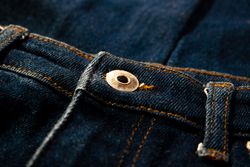 Close up gold and shiny button navy blue jeans fabric background texture.
