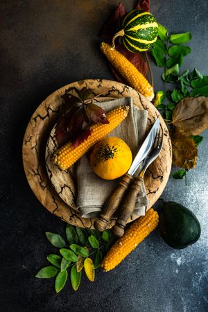 Top view of rustic autumnal table setting with mini squash, corn and leaves