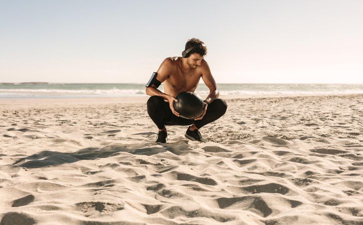 Man doing fitness workout at a beach using a medicine ball