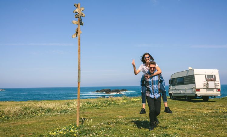 Young man piggybacking his girlfriend near the coast