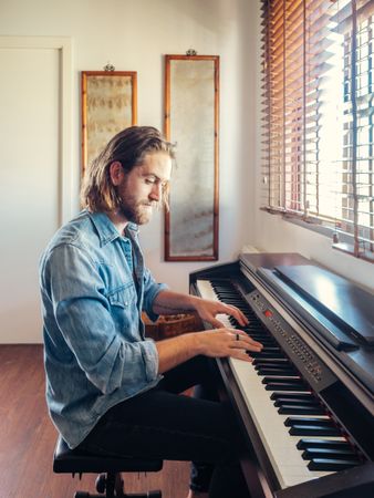 Wistful male playing synthesizer by window in flat