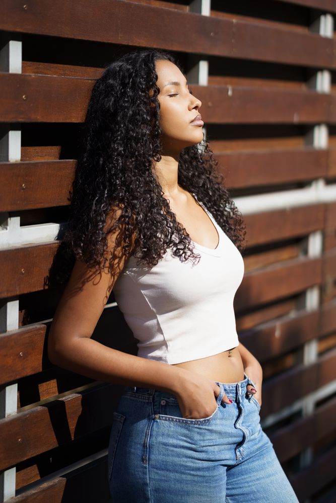 A Stylish Young Woman Posing Gracefully Against a Wooden Fence in the Bright Sunlight