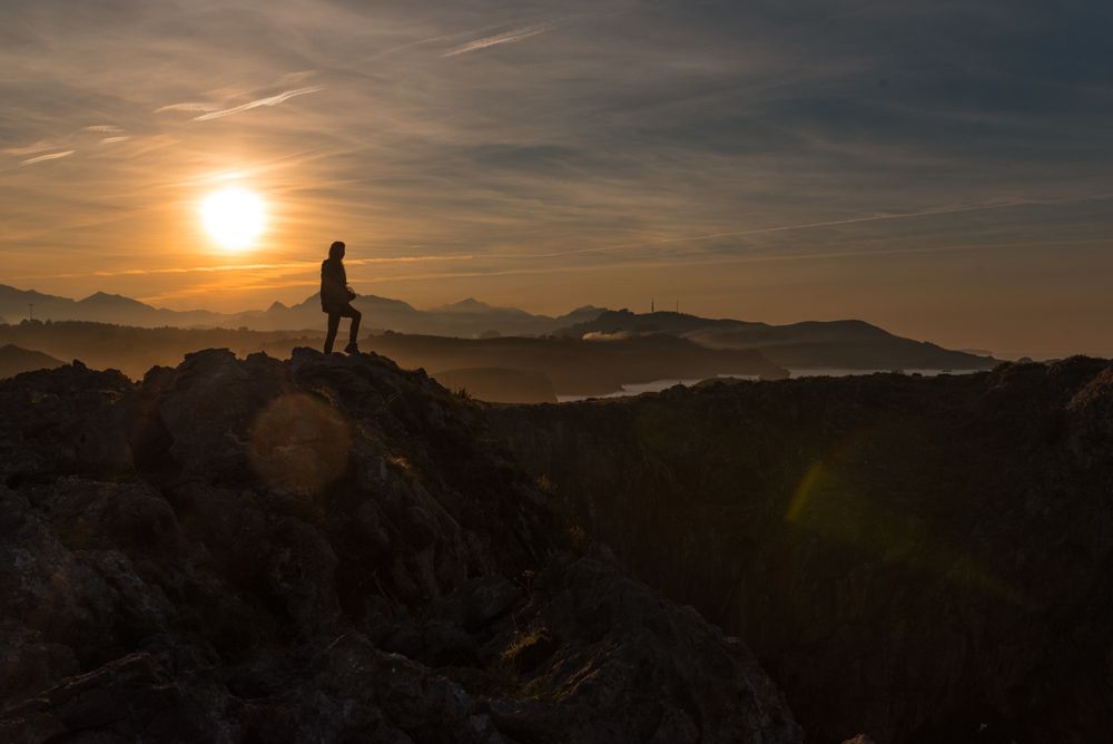 Traveler on high coastal cliff in sunset