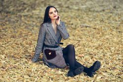 Content female relaxing in park in fall time with colorful leaves on ground looking away