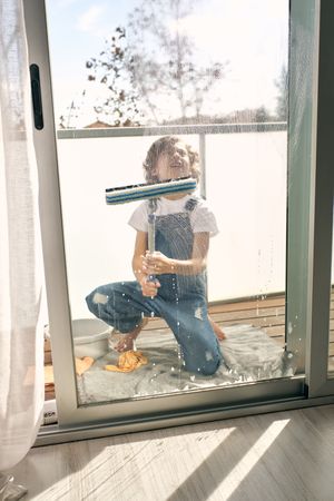 Preteen boy cleaning windows with mop at home