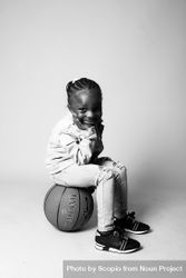 Grayscale photo of girl sitting on basketball against light background 5oKOk5