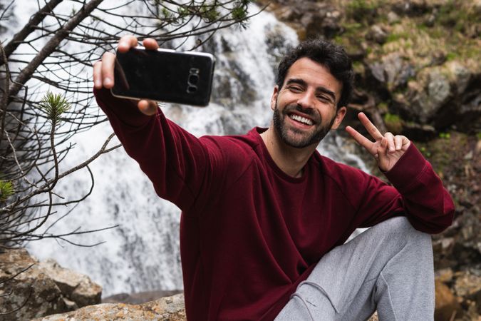 Delighted traveling man taking selfie against waterfall