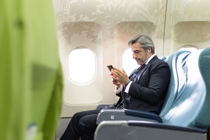 Grey haired male using smartphone in flight