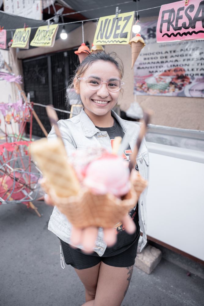 A young Hispanic woman is smiling holding a traditional ice cream in front of a street market stall