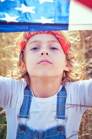 Preteen boy covering head with American flag in nature