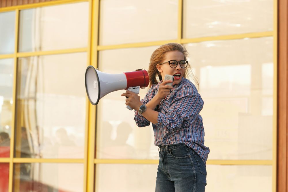 Woman yelling into megaphone in checkered shirt