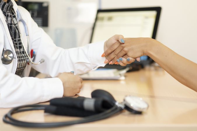 Doctor holding hand of patient at table with pulsometer