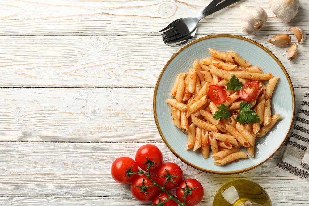 Composition with plate of tasty pasta and ingredients for cooking on wooden background