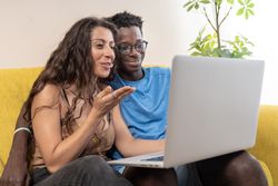 A happy diverse couple on a video call with family, the woman is blowing a kiss to the laptop screen.