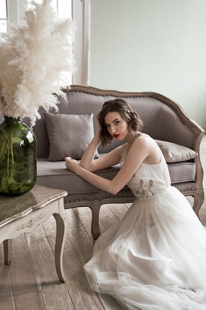 woman with red lips in white dress looking at camera while sitting on floor beside sofa