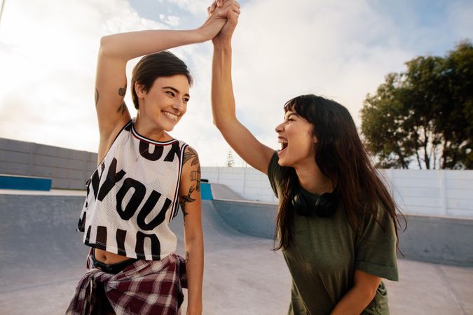 Two excited female friends high fiving at skate park